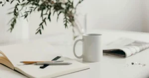 ノートとペン、白いマグカップが置かれた落ち着いたデスクで家計管理の準備をしている様子