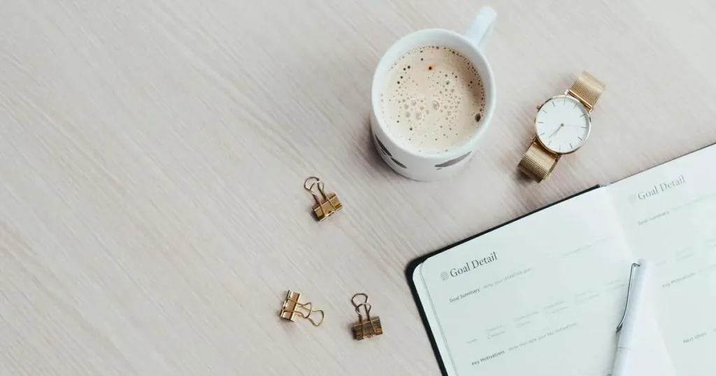 ノートとコーヒー、腕時計が整然と置かれたデスクで資産計画の整理をしている様子