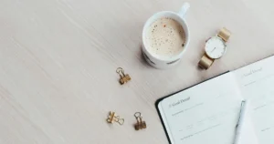 ノートとコーヒー、腕時計が整然と置かれたデスクで資産計画の整理をしている様子